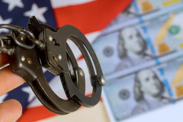 Handcuffs held firmly with counterfeit US money in background serious mood reflects caution apprehension