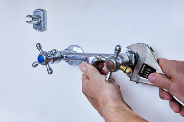 Detaching outdated faucet to install modern fixture, person uses wrench to unscrew metal tap with...