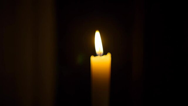 Illuminated wax candle with bright flame burning in the dark for memorial, celebration, religious observance, or relaxation purpose.