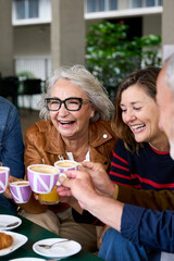 Vertical. Group laughing mature people having snack sitting at cafe bar. Older friends toasting with coffee cups gathered together in terrace restaurant. Food and beverage lifestyle in senior citizens