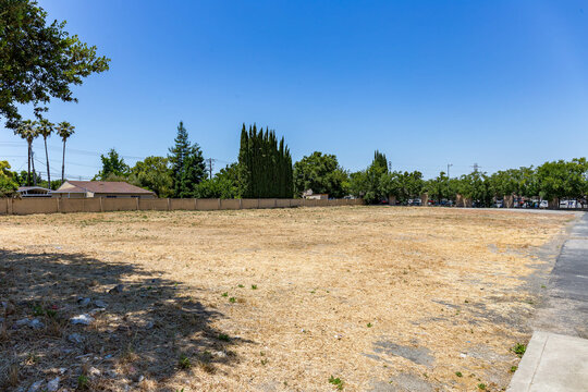 Vacant lot in a suburban Antioch, California neighborhood on a sunny day. The dry land and sparse grass suggest development potential or urban infill opportunity near residential housing.