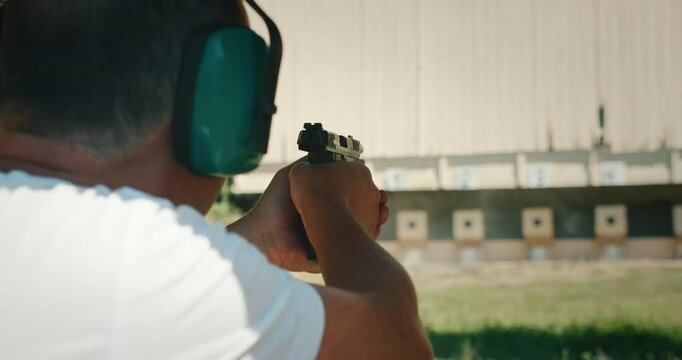 Man firing handgun pistol at targets with ear protection while shell casing ejecting at shooting range