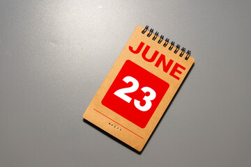Wooden block calendar with date June 23 on white concrete background.