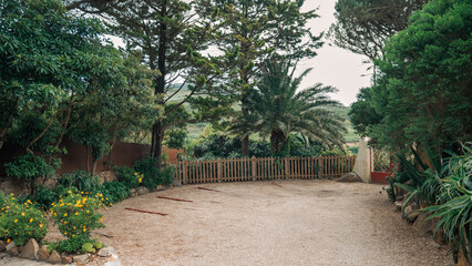 Obraz premium Secluded gravel parking area in a remote countryside location, surrounded by lush tropical vegetation, tall trees, and a wooden fence, creating a peaceful and natural setting