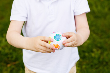 Child holding a multicolored sensory puzzle ball toy in hands, close-up view on green outdoor...
