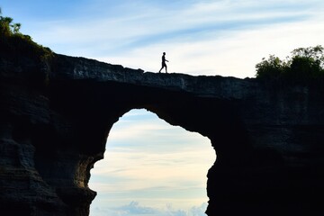 Silhouette of person walking on natural rock arch bridge