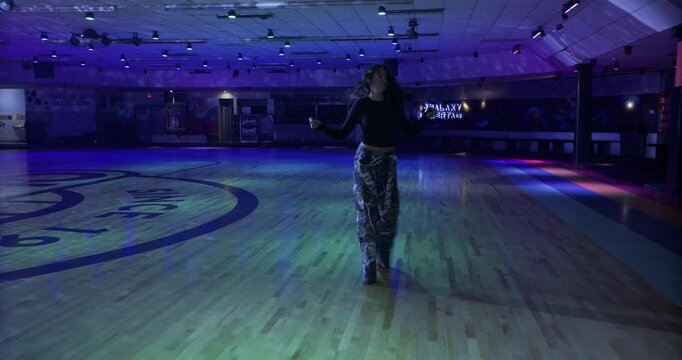Beautiful young woman dancing across wood floor on roller skates alone - wide, steady cam shot
