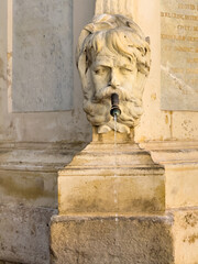 Aix-en-Provence, France - July 10, 2024: Fontaine de l'eau benite, holy water, on Place de l'hotel de ville. Detail showing water flowing out of the mouth of the male head sculpture