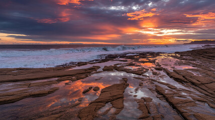 Obraz premium Vibrant sunset over ocean waves crashing on rocky shore