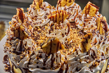 Typical showcase cake of a Latin American pastry shop torta tres leches topped with creamy frosting, chocolate drizzle, and crunchy cookie pieces, delightful dessert experience in cozy cafe atmosphere