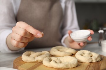 Woman adding sea salt onto uncooked pretzels at table indoors, closeup