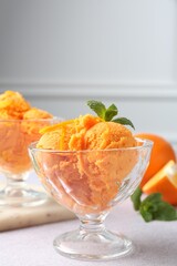 Tasty orange sorbet, fresh fruits and mint on light grey table, closeup
