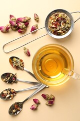 Delicious herbal tea in glass cup and dry leaves on beige background, flat lay