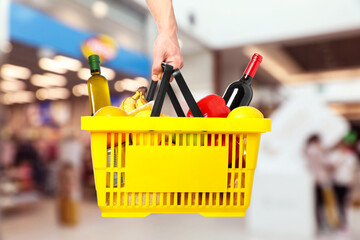 Man holding shopping basket with different food products at supermarket, closeup