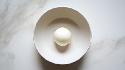 A single boiled egg in a white bowl on a marble surface