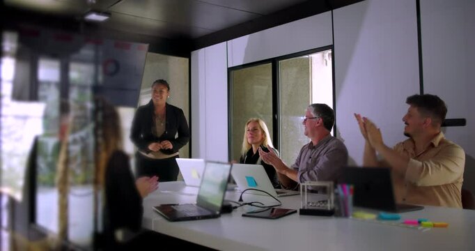 Colleagues applauding African American presenter after presentation in bright modern conference room with laptops and digital charts