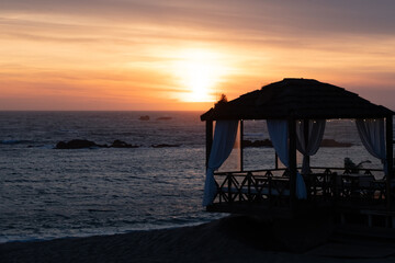 Cosy beach restaurant in silhouette at sunset with beautiful vivid golden sky.