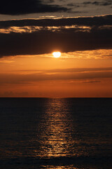 Sunset over the ocean, vertical background image. Setting sun appearing from behind clouds.