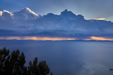 A dramatic stormy sky looms over the vast expanse of Lake Titicaca, casting deep shadows and rich blues across the high-altitude landscape.