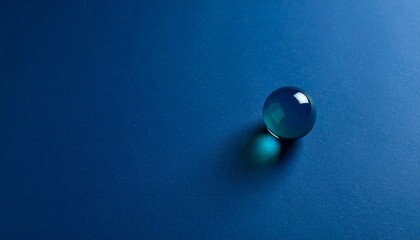 深いネイビーブルーのマット背景に小ぶりな青緑色ガラス玉が右下隅で輝き、静謐な空間と抽象的な美意識を共存させるデザイン。

