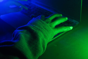 Person using laptop with green and blue lighting at night, cyber crime concept 