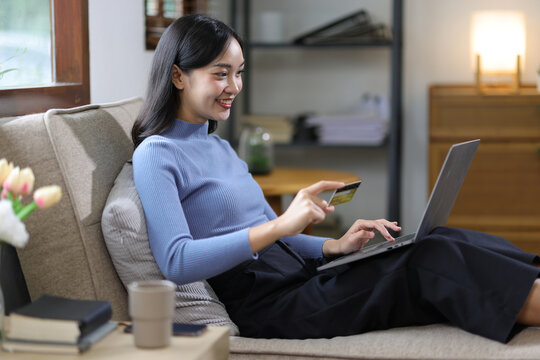 Young Asian woman at home happy doing online shopping on laptop and paying with credit card.