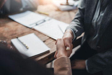 Businesswomen engaging in a handshake over a wooden desk after finalizing a contract in a...