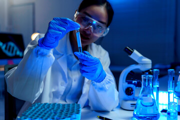 Scientist wearing protective glasses and gloves carefully examining test tube with blue liquid,...