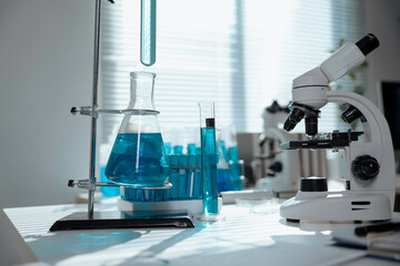 Glassware containing blue chemical liquid is standing on table near microscope in modern laboratory