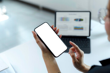 Businesswoman holding smartphone with blank white screen while working with tablet showing graphs in office