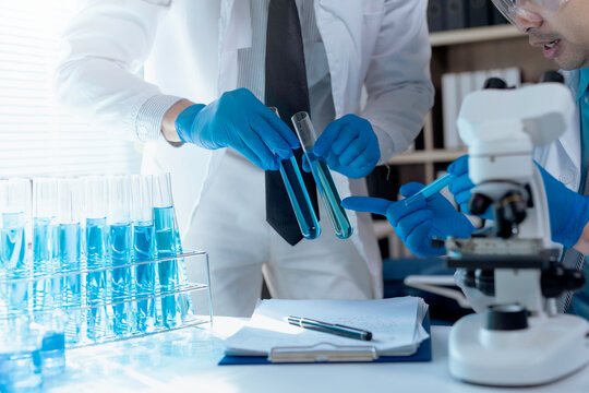 Two scientists wearing lab coats and gloves comparing test tubes with blue liquid during an experiment in a laboratory