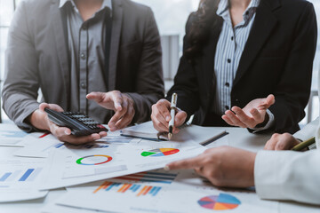Business people analyzing financial charts and discussing data at office desk, using calculator and pen, teamwork concept