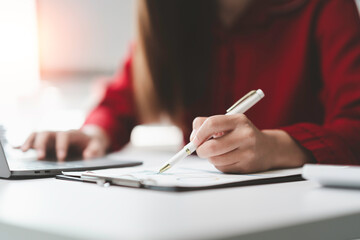 Businesswoman working diligently at her office desk, analyzing documents and utilizing a laptop to...