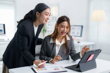 Two asian businesswomen are discussing and analyzing charts on digital tablet and paperwork in modern office