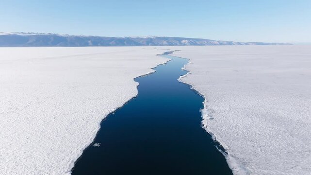 Aerial view of a crack with water in the icy frozen surface, sunny spring day