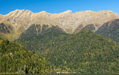 Lake Ritsa, near the mountain peaks, is surrounded by dense forests on the slopes. A warm autumn day in October gives the lake a special charm.