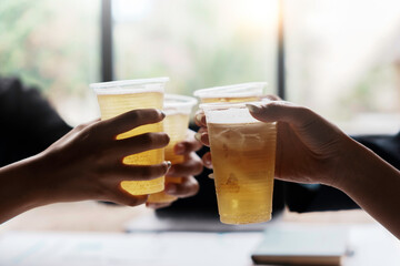 Coworkers raising plastic cups filled with beer, celebrating a successful business deal and enjoying a moment of teamwork and achievement