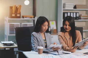 Two young Asian business woman talk, consult, discuss working with new startup project idea presentation analyze plan marketing and investment in the office.