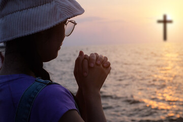 Christian woman praying in the sky with cross and light