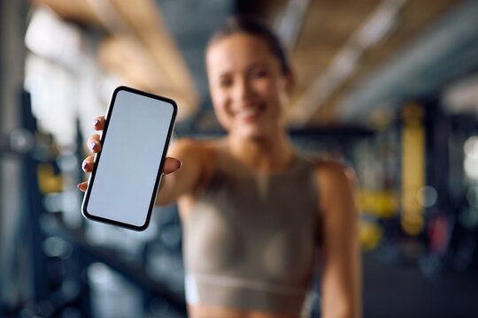 Close up of sportswoman holding smart phone with blank screen in gym.