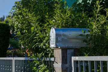 Mailbox in a Lush Garden. A silver mailbox surrounded by green foliage on a sunny day