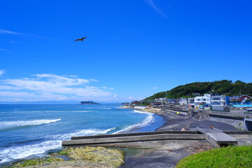 サーファーが波と戯れる夏真っ盛りの湘南・鎌倉の海と、美しい江ノ島の風景で、夏休みのイメージ
