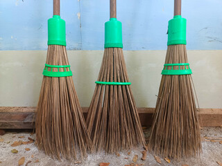 Three brooms are made from coconut tree fronds tied and attached to a handle.