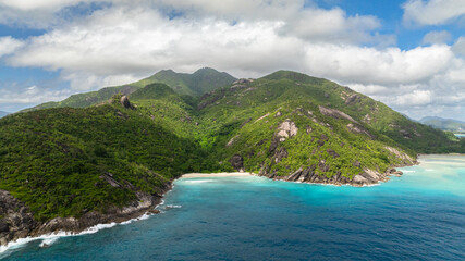 Secluded beach surrounded by lush green hills and turquoise water. Seychelles, Mahe. Anse Du Riz beach. Baie Ternay Marine National Park.