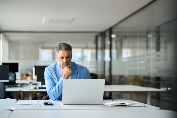 Busy serious middle aged professional business man financial investor, 50 years old senior businessman executive wearing suit using laptop computer working on investment plan at office desk.