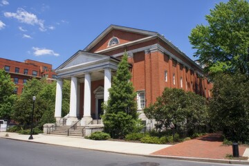 Front view of historic red brick building with white columns and grand entrance, lush greenery and blue sky, classic American urban architecture