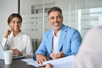 Smiling older male manager working with colleagues in office, consulting client or investor,...