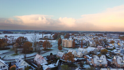 Drone winter aerial shot of houses with solar panels snow on roof during sunset. Street in a...