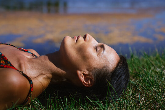 Serene woman relaxing and lying on a grass next to the pond