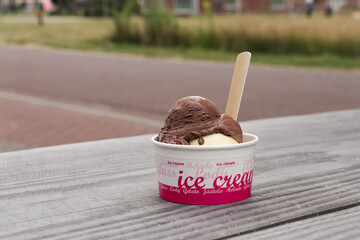 Chocolate ice cream cup on wooden table outside. Summer treat, fun snack. Icecream flavors with environmentally friendly spoon.